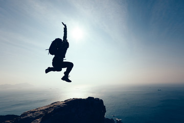 free female hiker jumping on sunrise seaside cliff edge