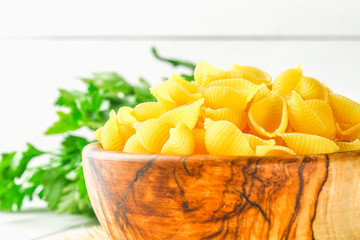 Culinary background with conchiglie pasta on wooden table. Pasta in the form of cockleshells in a wooden bowl with parsley.