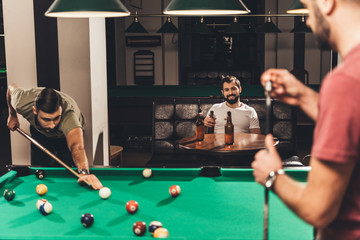 group of young successful handsome men playing in pool at bar