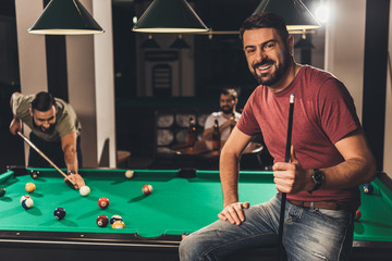 young handsome caucasian man beside billiard table in bar with friends