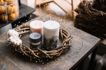 Beautiful festive hand-made candles (with concrete in it) and a wooden florist wreath around it with firefly garland on a rustic old wooden table with festive decoration on the background