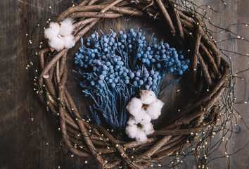 Blue berries and cotton inside a hand-made wooden wreath with a fireflies garland around it, on a rustic wooden table background, flat lay