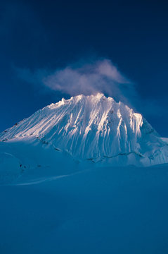 Alpamayo, one of the most beautiful mountain views on earth catching the last light at sunset with clouds above its icy and snowy face