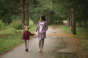 Fototapeta premium A young mother and her little daughter are walking along the path in the park
