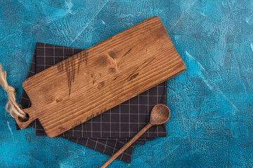 Chopping board with kitchen towel and wooden spoon on blue background with copy space for text