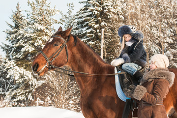 Small girl and mom near horse in a winter