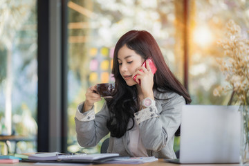 Obraz premium Young Asian female entrepreneur talking on the phone while working at home office. 