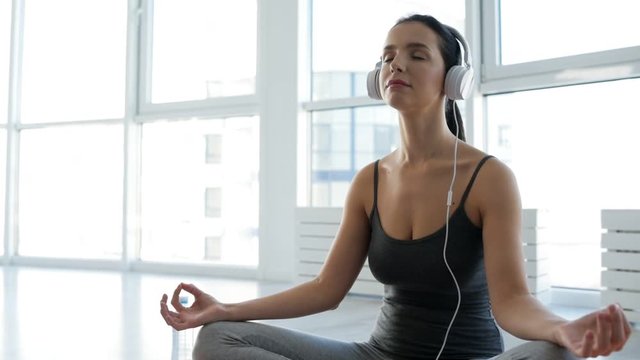 Mind peace. Close up of adorable young woman sitting in yoga position while listening to music and doing meditation
