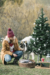 Woman and her dog having fun outdoor while decorating a Christmas tree