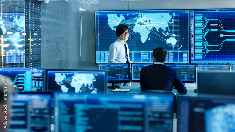Poster In the System Control Room Chief Engineer Holds a Briefing for Member of the Staff. They're Work in Data Center and are Surrounded by Multiple Screens Showing Maps, Logistics Data.