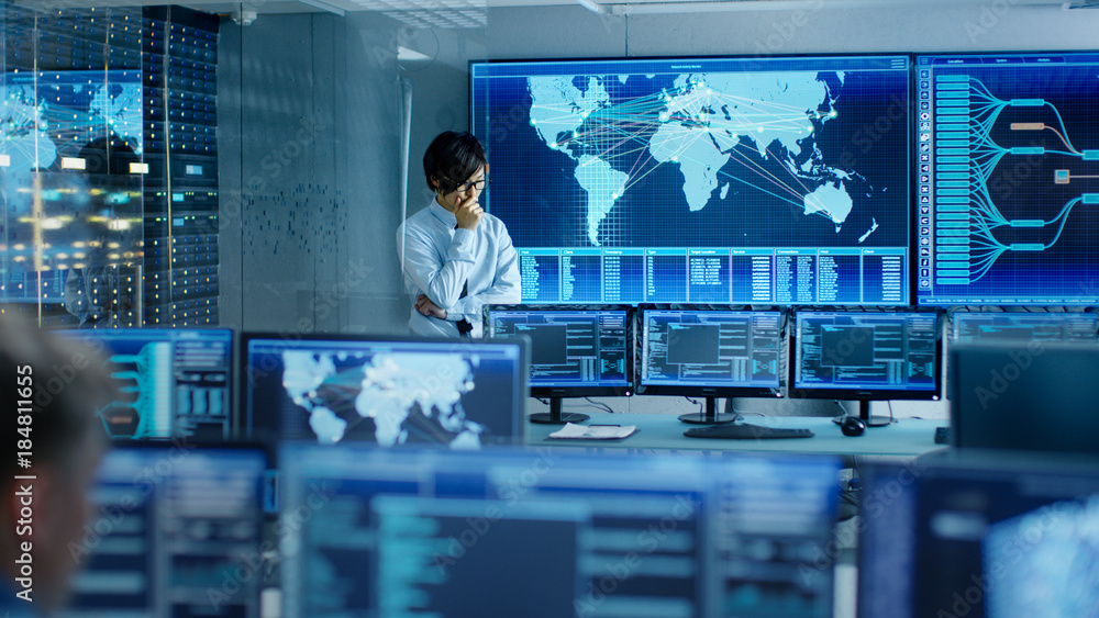 Poster In the System Control Room Chief Engineer Thinks While Standing Before Big Screen with Interactive Map on it. Data Center is Full of Monitors Showing Graphics.