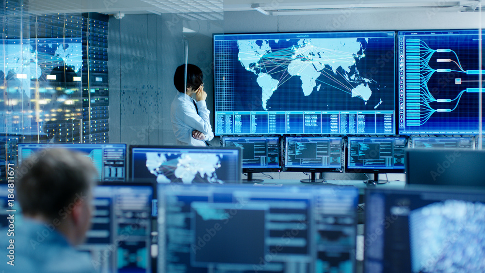 Poster In the System Control Room Chief Engineer Thinks While Standing Before Big Screen with Interactive Map on it. Data Center is Full of Monitors Showing Graphics.