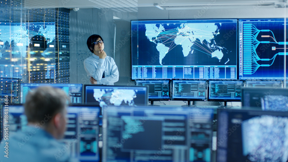 Poster In the System Control Room Chief Engineer Thinks While Standing Before Big Screen with Interactive Map on it. Data Center is Full of Monitors Showing Graphics.