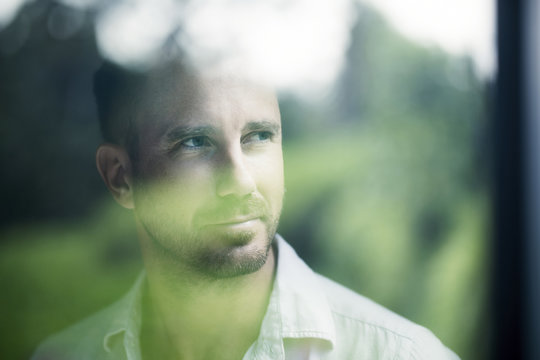 Attractive man looking through window pane, smiling, portrait