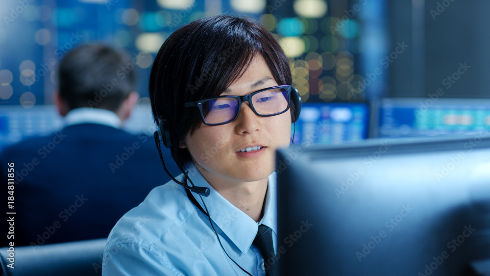 Poster In the Network Operations Center Senior Trader Teaches Young Associate to Makes Personal Client Call with a Headset. They're Surrounded by Monitors Showing Data and Graphs.