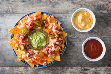 Mexican nachos with beef, guacamole, cheese sauce, peppers, tomato and onion in plate on wooden table. Top view
