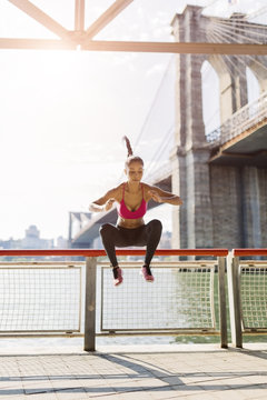 Female athlete training in Manhattan near Brooklyn Bridge, jumping mid air