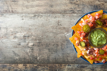 Mexican nachos with beef, guacamole, cheese sauce, peppers, tomato and onion in plate on wooden...