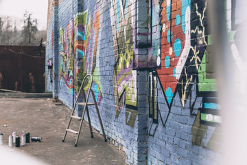 cans with spray paint and ladder near colorful graffiti on wall of building in city