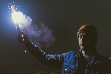 man holsing smoke bomb with sparks at night