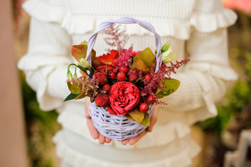 Woman in a white sweater holding a cute wicker basket with valentine flower composition