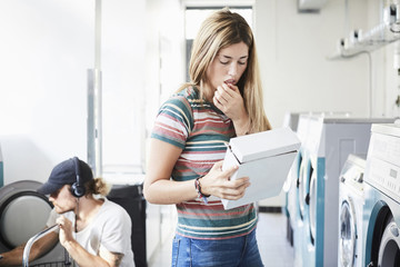 Woman reading information on detergent pack while man using washing machine at laundromat
