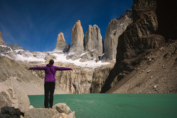 Young woman is embracing Torres del Paine towers with open arms in Patagonia region in Chile