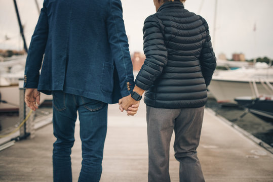 Midsection of senior couple holding hands while walking on pier at harbor