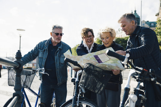 Senior male and female friends with bicycles reading map in city