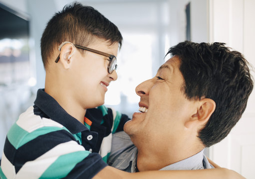 Close-up of happy father carrying smiling disabled son while standing at home
