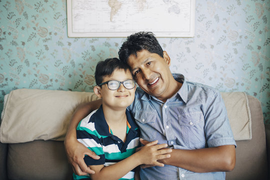 Portrait of smiling father and son sitting on sofa against wall at home