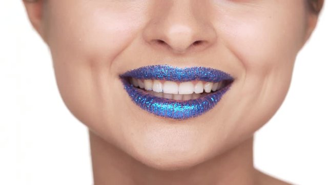 Extreme close up portrait of seductive female person 30s biting her lower lip covered with blue shining glitter having flirty emotions over white background. Facial expressions