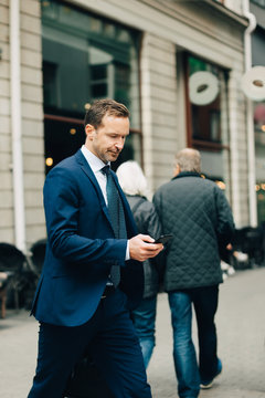 Mature businessman using smart phone while walking on sidewalk in city