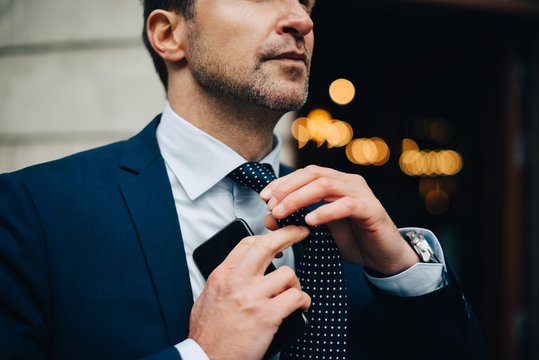 Midsection of businessman adjusting necktie while holding mobile phone