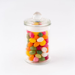 glass jar filled with candy and caramel with the lid closed on white background.