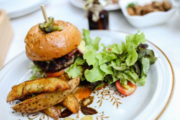 Burger full face with vegetables, spices and fries. Meat hamburger. Beef hamburger. decorative dish on table