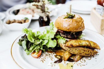 Burger full face with vegetables, spices and fries. Meat hamburger. Beef hamburger. decorative dish on table