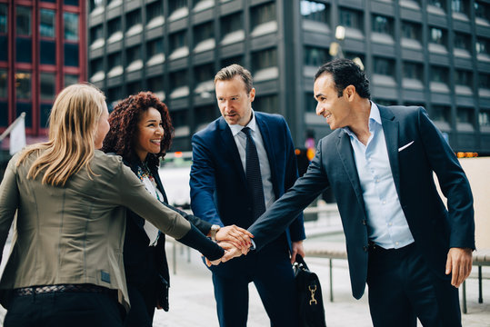 Smiling business people stacking hands against office building