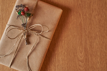 A book shaped present wrapped in brown paper and tied with brown paper thread with small dried bouquet of field plants in it.