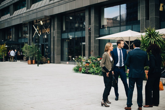 Full length of business colleagues talking while standing on footpath against building