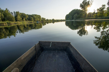 The bottom of the boat cuts the surface of the water. Entering a small dock for boats. The shores of the river are covered with lush vegetation. The surface of the water reflecting as a mirror.
