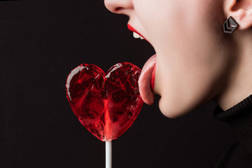 cropped image of woman licking heart shaped lollipop isolated on black