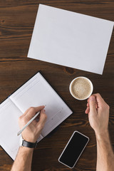 partial view of businessman making notes in notebook at table