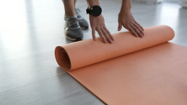 Starting training. Close up of young sportive woman unrolling the mat on the floor before practicing exercises