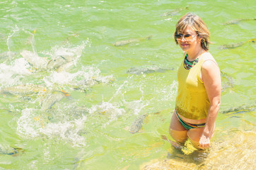Woman tourist seated on the margin of the river Formoso with some piraputanga fishes swimming on...