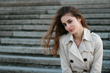 Pretty girl with long curly hair wearing beige fashionable coat over staircase background