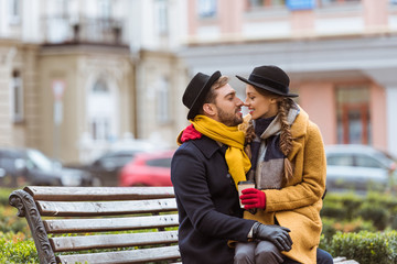 beautiful couple sitting on bench with coffee cup