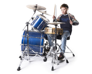young blond boy at drum kit in studio against white background