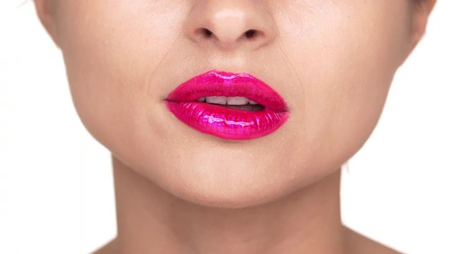 Extreme close up portrait of seductive female person 30s biting her lower lip covered with pink lipgloss being serious over white background. Facial expressions