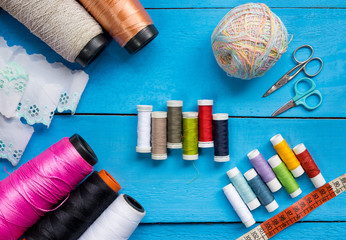 Colorful Sewing thread line spools, big and small, scissors, frill soft cloth and measuring tape on top of a blue wooden background tabletop, concept and idea